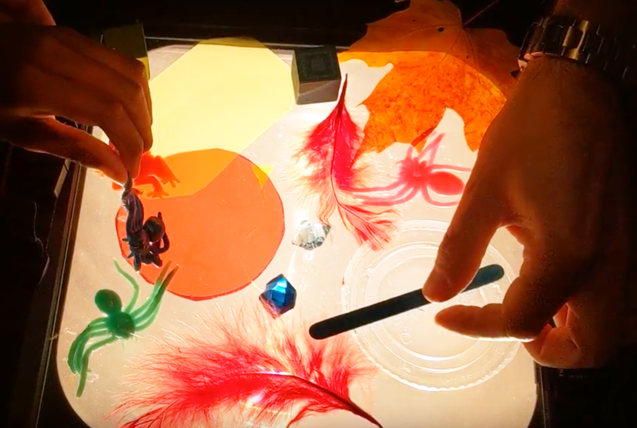 Child and facilitator exploring different craft items against a slide projector light. 